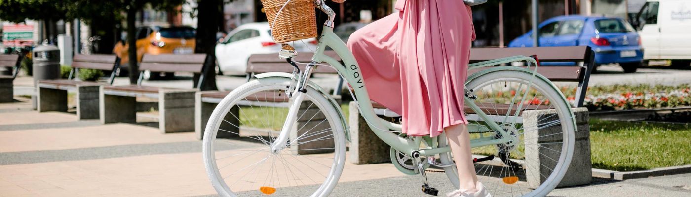 Kvinna i rosa klänning cyklar med korg.