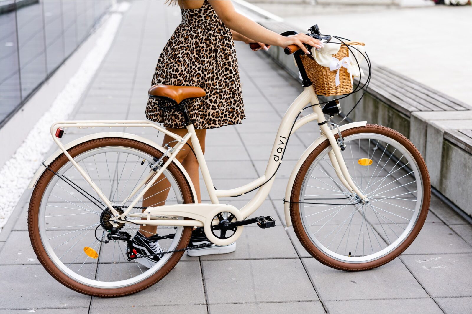 Kobieta w sukience przy rowerze na chodniku.