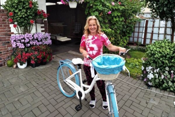 Kobieta z rowerem na tle kwiatów.